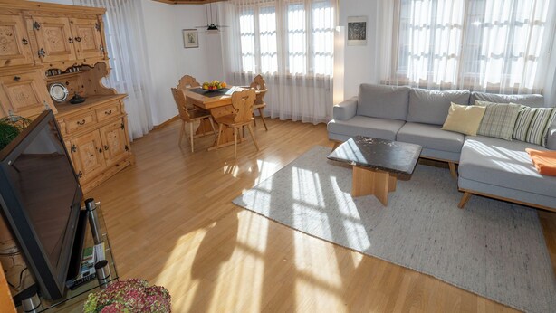 Un soggiorno con soffitto in legno, un divano, un tavolo da pranzo con sedie e una televisione.