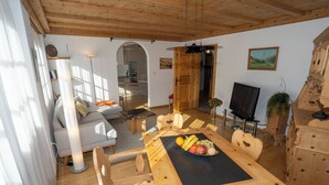 Un tavolo da pranzo in legno con frutta, una TV e un armadio in legno in una stanza luminosa con soffitto in legno.