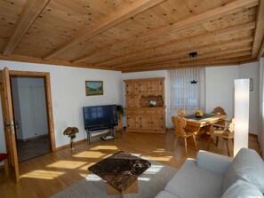 Una sala de estar con televisor, muebles de madera y un comedor con mesa y sillas.