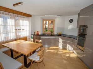 Eine moderne Küche mit einem Holztisch, einem eingebauten Ofen und einem großen Fenster mit transparenten Vorhängen.
