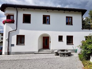 Ein zweistöckiges Gebäude mit weißer Fassade, zahlreichen Fenstern, einem zentralen Eingang mit Bogen und einem gepflasterten Auffahrt.