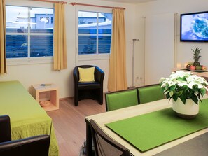 A room with a bed, a chair, a dining table, a television, and a window with curtains. - Schudel, (Scuol) by Interhome (Scuol)