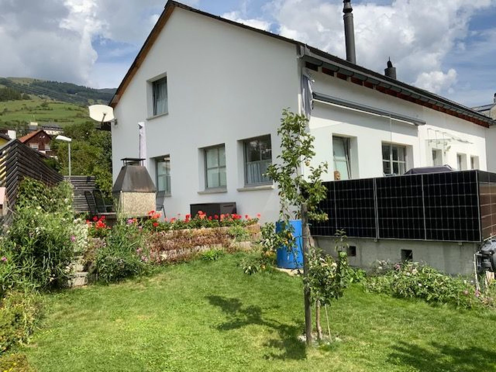 Ein modernes, zweistöckiges Haus mit weißer Fassade, einem Schornstein und einer Solaranlage.