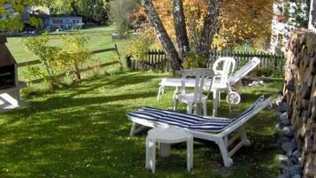 Eine Terrasse mit Tisch und zwei Liegestühlen, umgeben von einer Rasenfläche und Bäumen.