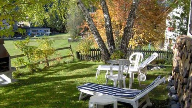 A patio with two white lounge chairs and a table, surrounded by a grassy lawn and trees with autumn foliage. - Chasa Quirin, (Zernez) by Interhome (Zernez)