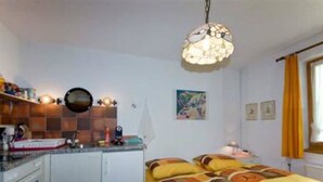 A compact room with a kitchenette, a bed with a patterned bedspread, a hanging light fixture, and a painting on the wall. - Chasa Quirin, (Zernez) by Interhome (Zernez)
