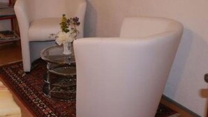 A room with a white armchair, a small round table with a vase of flowers, and a patterned rug. - Chasa Quirin, (Zernez) by Interhome (Zernez)