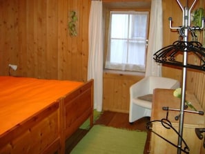 A room with a wooden bed, a white chair, a radiator, and a window with curtains.