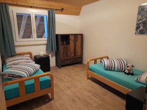 Una habitación con dos camas de madera, un armario y una ventana con cortinas.