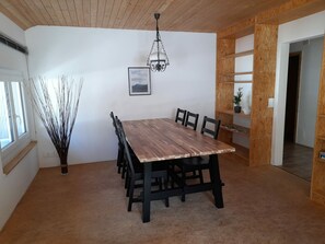 A dining area with a wooden table and chairs, a hanging light fixture, a framed picture on the wall, and a potted plant on a shelf. - Ferienwohnungen Paclerahof, (Sta. Maria - Santa Maria Val Müstair) by Interhome (Sta. Maria GR)
