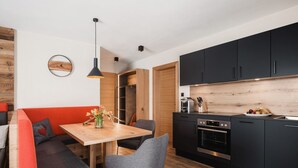 A modern kitchen with black cabinets, a wooden dining table, and a built-in oven. - Avero Lodge by MEIN SAMNAUN – MOUNTAIN HOMES, (Samnaun-Compatsch) by Interhome (Samnaun)