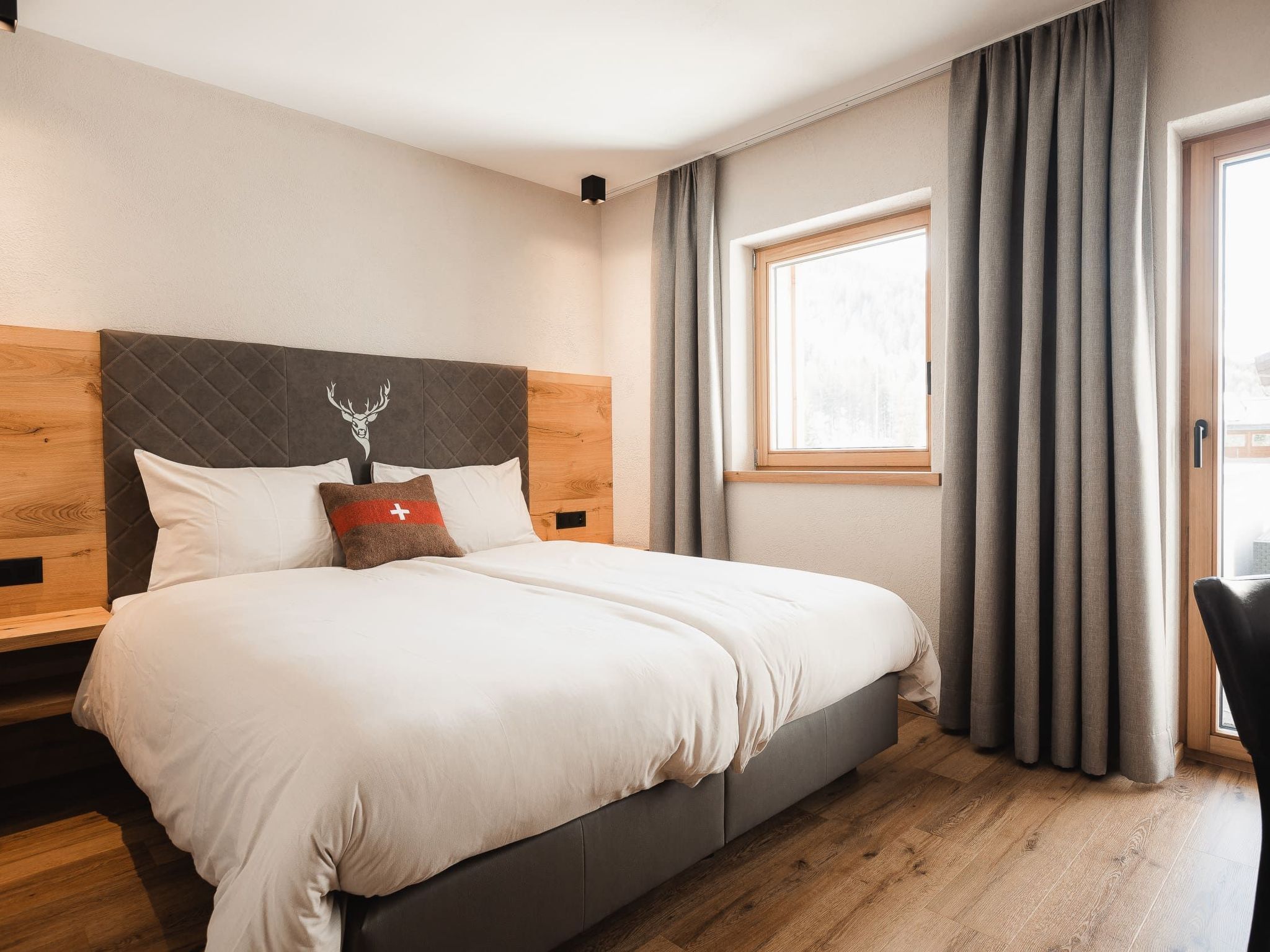 Camera da letto moderna con un letto grande, una testiera in legno, una finestra con tende e un pavimento in legno.