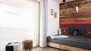 A cozy room with a wooden floor, a grey sofa with red cushions, a small stool, and a wooden wall with a mounted animal skull. - Avero Lodge by MEIN SAMNAUN – MOUNTAIN HOMES, (Samnaun-Compatsch) by Interhome (Samnaun)