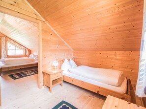 Ein Holzhütten-Zimmer mit einem Schlafplatz auf Hochbett, einem Nachttisch mit Lampe und einem Fenster.