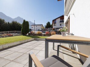 A patio with a table and chairs, a flower pot, and a view of houses and mountains in the background. - Wieser, (Sent) by Interhome (Sent)