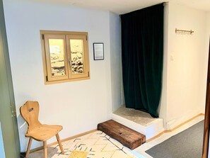 A room with a wooden chair, a window with a view, a dark curtain, and a small wooden bench. - 3-Zimmerwohnung Chasa d'Uina, (Sent) by Interhome (Sent)