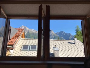 Ein Fenster mit Blick auf ein Gebirge und ein Gebäude mit einem Ziegeldach.