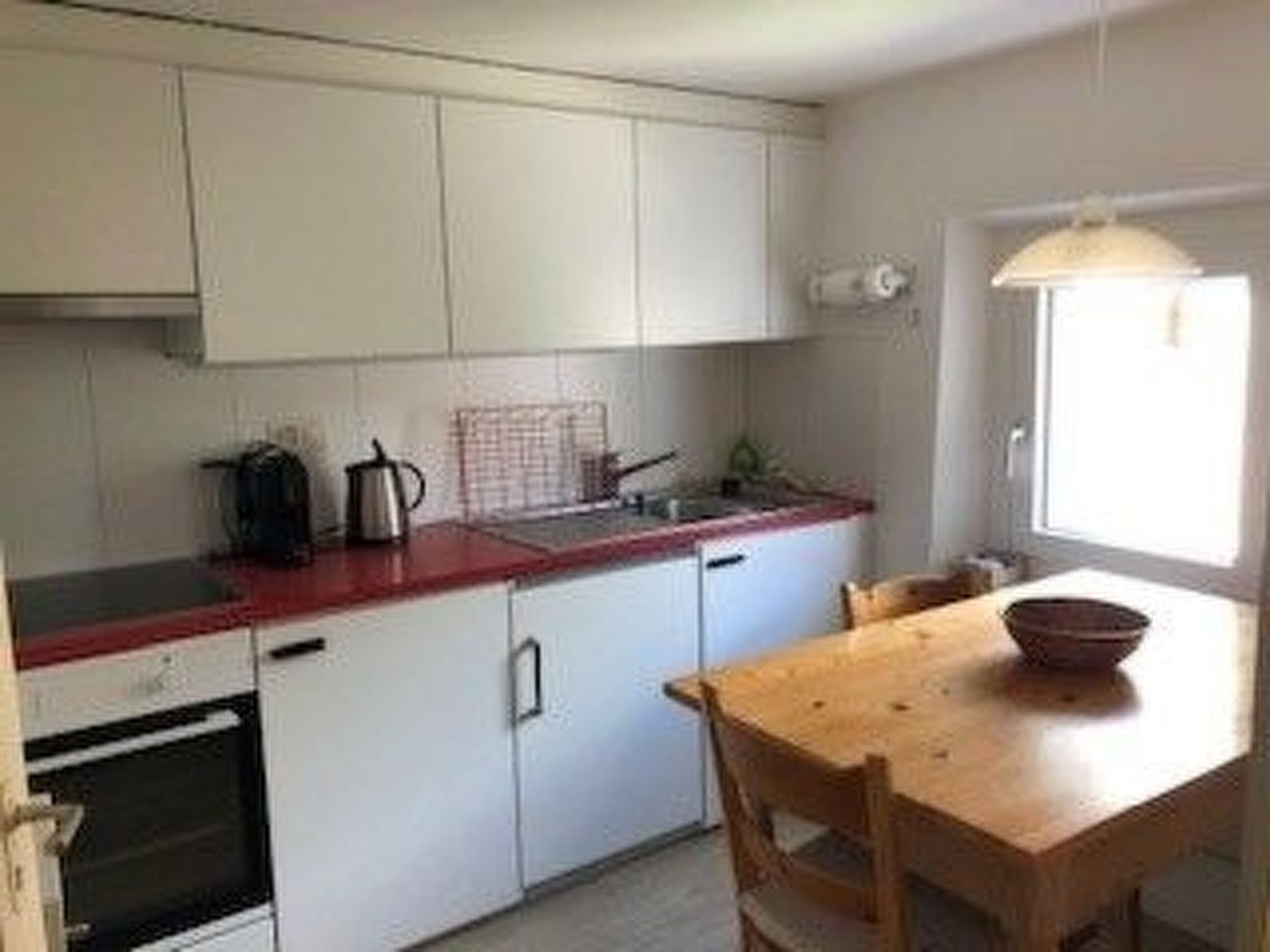 Une cuisine compacte avec des meubles blancs, un plan de travail rouge et une table à manger en bois.