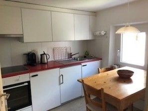 Eine kompakte Küche mit weißen Schränken, einer roten Arbeitsplatte und einem Holztisch.