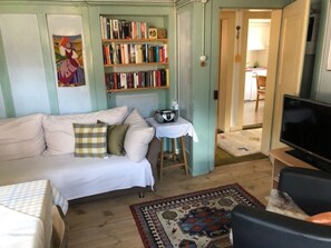 Un salon confortable avec un canapé, une petite table sur laquelle se trouve une radio, une bibliothèque et un téléviseur.