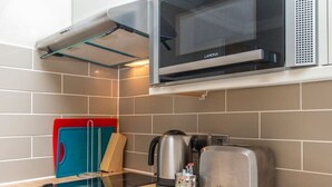 Eine Küche mit Mikrowelle, Toaster, Wasserkocher und einem Schneidebretthalter.