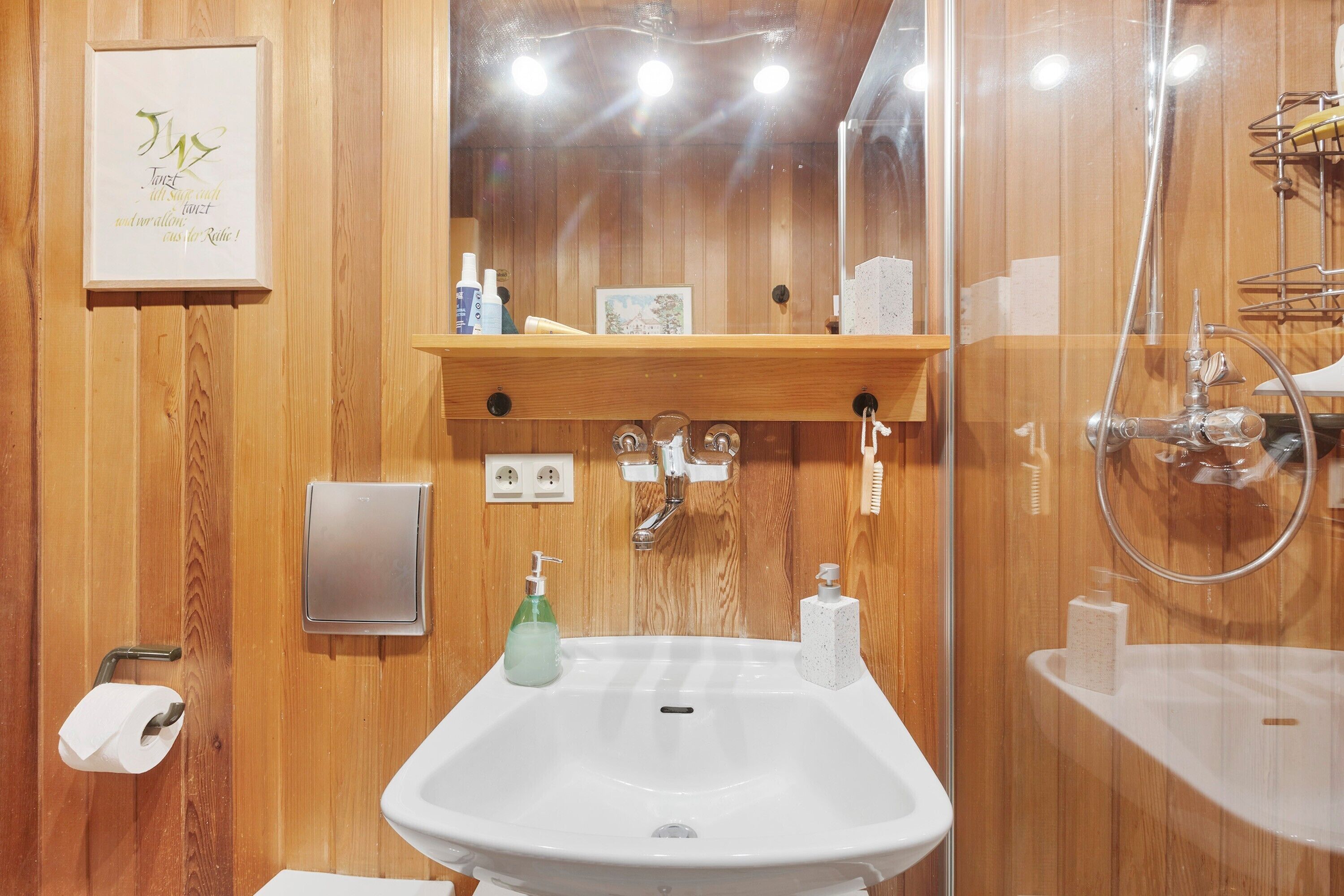 Une salle de bain avec des lambris en bois, un lavabo, un miroir, une douche et une étagère contenant des articles de toilette.