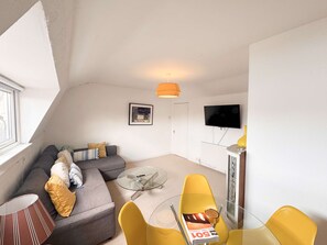 A modern living room with a sofa, a glass coffee table, and yellow chairs. - One Bed Apartment in Clifton (Bristol)