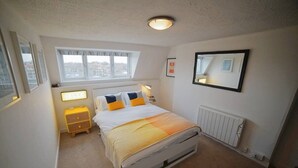 Ein Schlafzimmer mit Bett, Nachttischen, einem Fenster, einer Heizung und einem Spiegel.