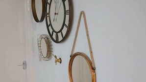 Ein Flur mit einer weißen Tür, einer weißen Bank und einer Wand, die mit verschiedenen Spiegeln und einer kleinen goldenen Lampe verziert ist.