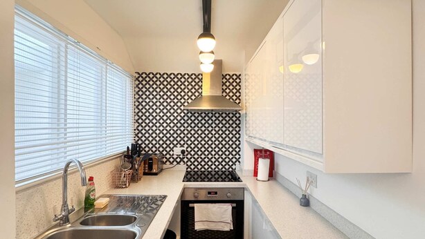 Eine kompakte Küche mit modernem Design, ausgestattet mit einem Edelstahl-Spülbecken, einem eingebauten Backofen und einer gemusterten Spritzschutzwand.