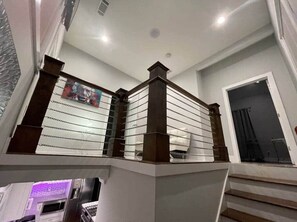 A staircase with a wooden handrail and glass balustrade, leading to a landing with a door and a window. - 1932 Relax in East Lake - Modern Retreat - Vacation Home in DeKalb County (Decatur)