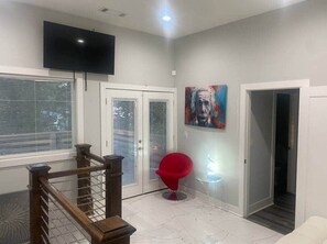 A room with a TV, a red chair, a painting, and a staircase. - 1932 Relax in East Lake - Modern Retreat - Vacation Home in DeKalb County (Decatur)