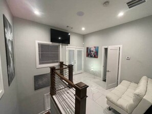 A spacious living area with a staircase, a flat-screen TV, a white sofa, and a painting on the wall. - 1932 Relax in East Lake - Modern Retreat - Vacation Home in DeKalb County (Decatur)