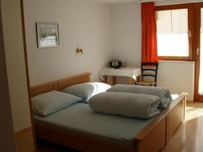 Ein Einzelbett mit Kissen, ein Nachttisch mit Radio und ein Stuhl.