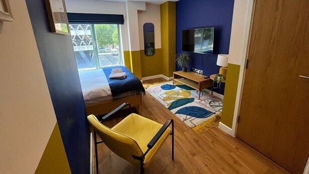 A room with a bed, a desk, a chair, a TV, and a door. - Prince Street Studio 7 (Bristol)