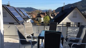 En terrass med ett bord och stolar, solpaneler på taket och utsikt över hus och kullar.