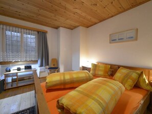 Ein Zimmer mit Holzboden, einem Bett mit orangefarbener Bettwäsche, einem Schreibtisch mit Stuhl und einem Fenster mit Vorhängen.