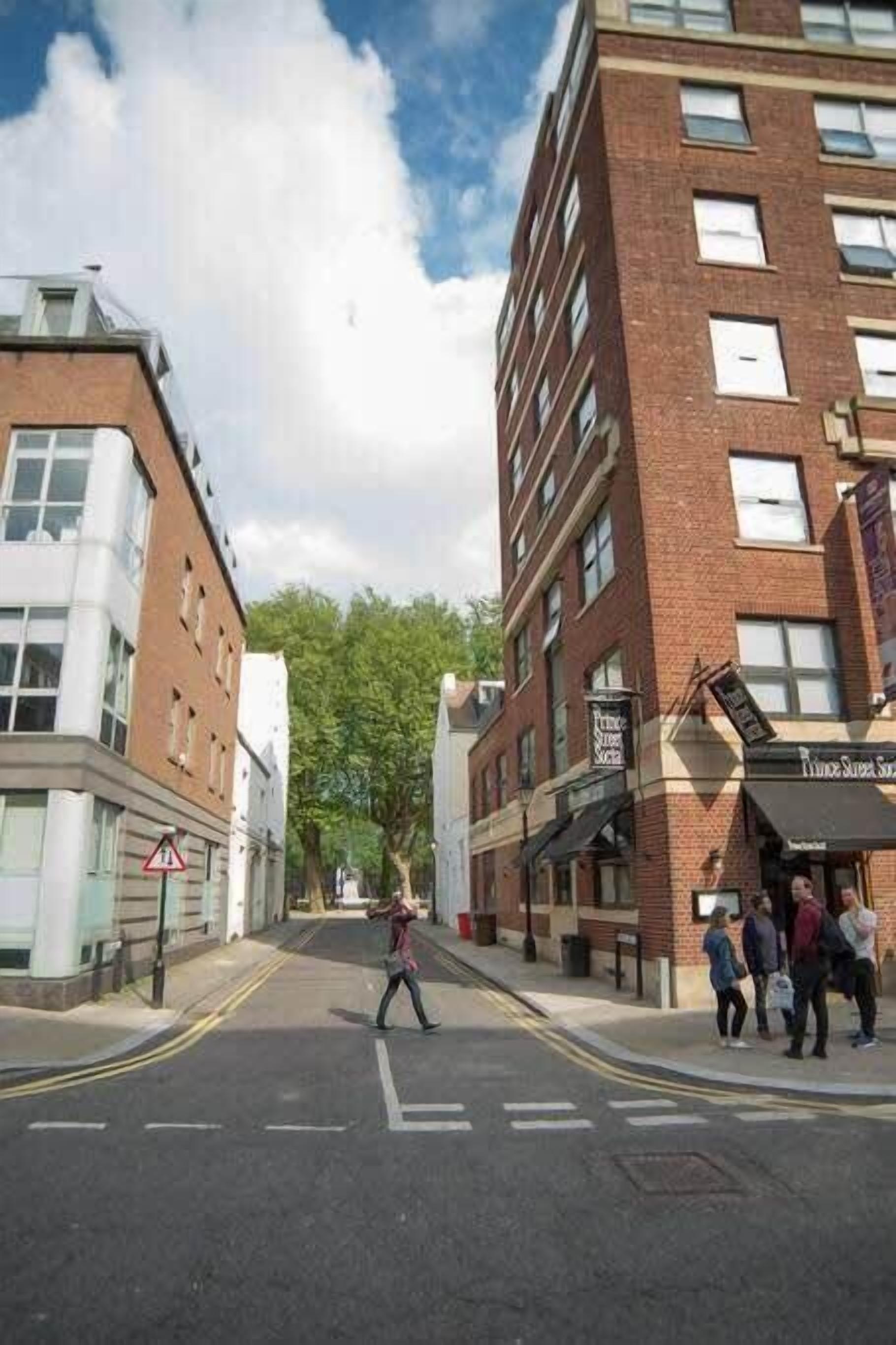 Une rue bordée d’immeubles, avec un passage piéton et un panneau indiquant une zone scolaire.