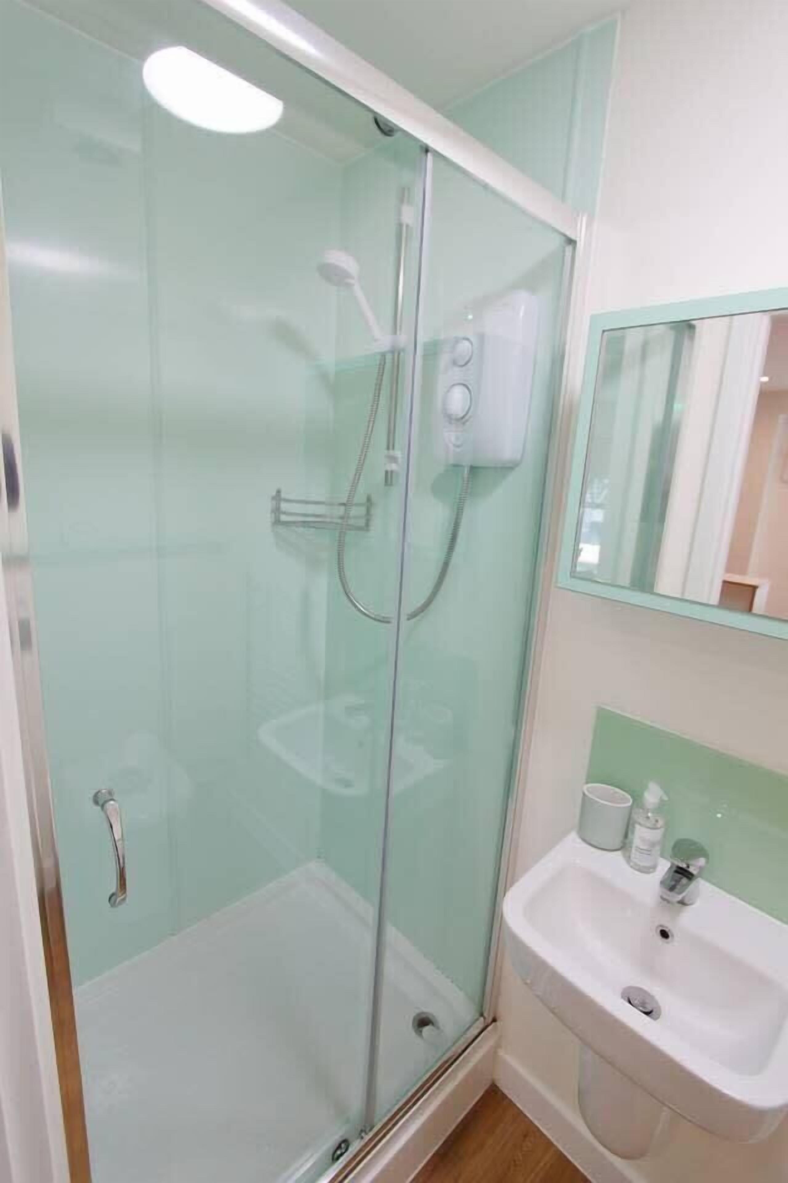 Ein Badezimmer mit Duschkabine, Waschbecken und Spiegel.