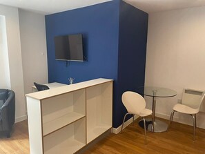 A room with a white desk, a TV mounted on the wall, a round glass table with two white chairs, and a black trash bin. - Prince Street Studio 6 (Bristol)
