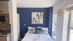 A bedroom with a bed, pillows, a painting, a clock, and a window. - Prince Street Studio 6 (Bristol)