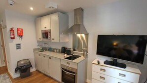 Una cocina compacta equipada con microondas, horno, pileta y un televisor de pantalla plana sobre un pedestal.