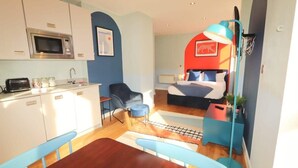 A compact hotel room with a kitchenette, a bed with a red headboard, a blue chair, and a small table. - Prince Street Studio 9 - Hopewell (Bristol)