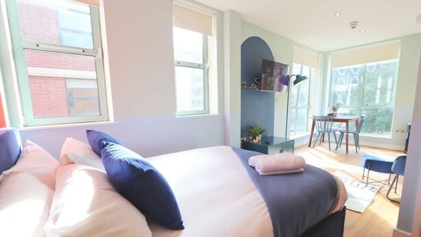 A bedroom with a bed, a desk, and a chair, and a view of a building outside. - Prince Street Studio 9 - Hopewell (Bristol)