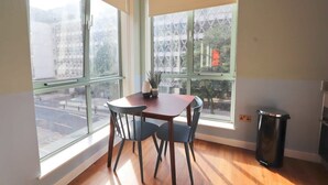 A room with a dining table and chairs, large windows, and a trash bin. - Prince Street Studio 9 - Hopewell (Bristol)