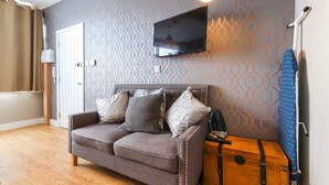 A room with a grey sofa, a mounted TV, a wooden trunk, and a patterned wall. - Old Market Studios-No1 (City of Bristol)