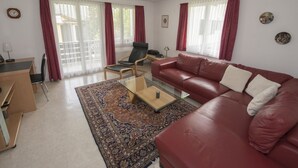 A living room with a red sofa, a glass coffee table, a wooden desk, and a patterned rug. - STEINMANN, (Scuol) by Interhome (Scuol)