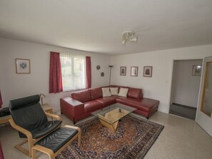 Ein Wohnzimmer mit einem roten Ledersofa, einem Glastisch, einem gemusterten Teppich und einem schwarzen Ledersessel.