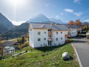 Un immeuble résidentiel moderne à deux étages, doté d’un toit en pente, de nombreuses fenêtres et offrant une vue sur une chaîne de montagnes en arrière-plan.