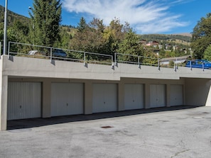 Une rangée de portes de garage fermées, surmontée d’une rambarde métallique, intégrée à une structure en béton, avec un ciel dégagé et des collines en arrière-plan.